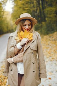 Woman posing for a photo in the autumn park. Caucasian girl has red lips. Woman wearing beige coat and a hat.